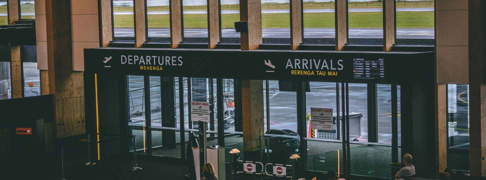 Busy airport terminal area with people, featuring departures and arrivals signs.