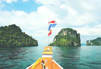 Long-tail boat sailing towards lush islands in the Andaman Sea on a sunny day.